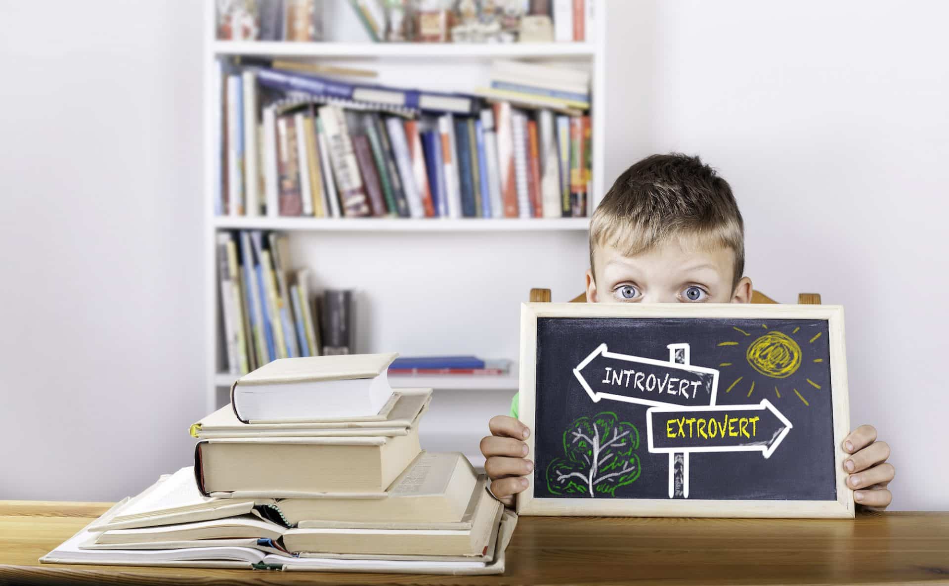 An introverted boy holding up a chalkboard with a directional sign.