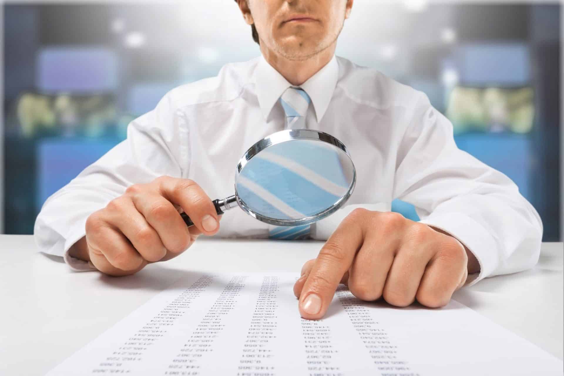A man, caught in the grips of perfection paralysis, intently examines a document through a magnifying glass.