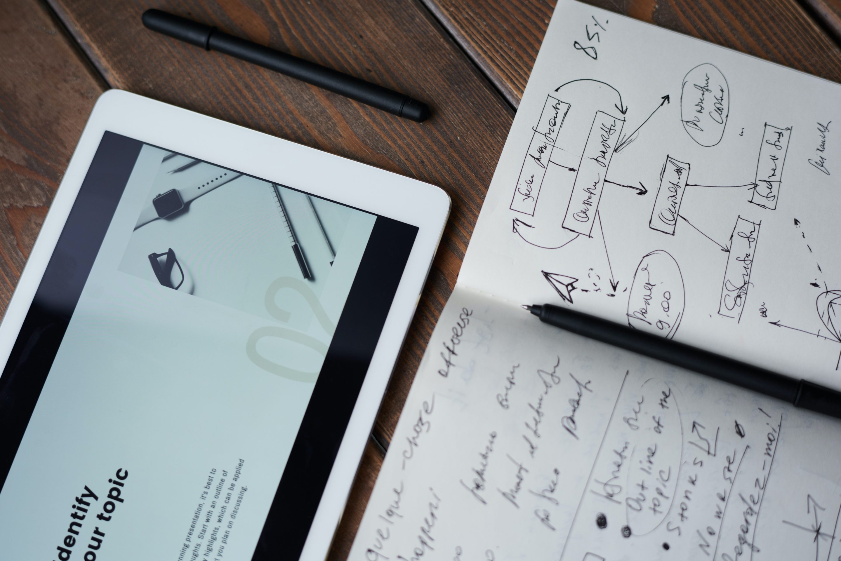 A tablet displaying engaging content, alongside a notebook and pen on a wooden table.