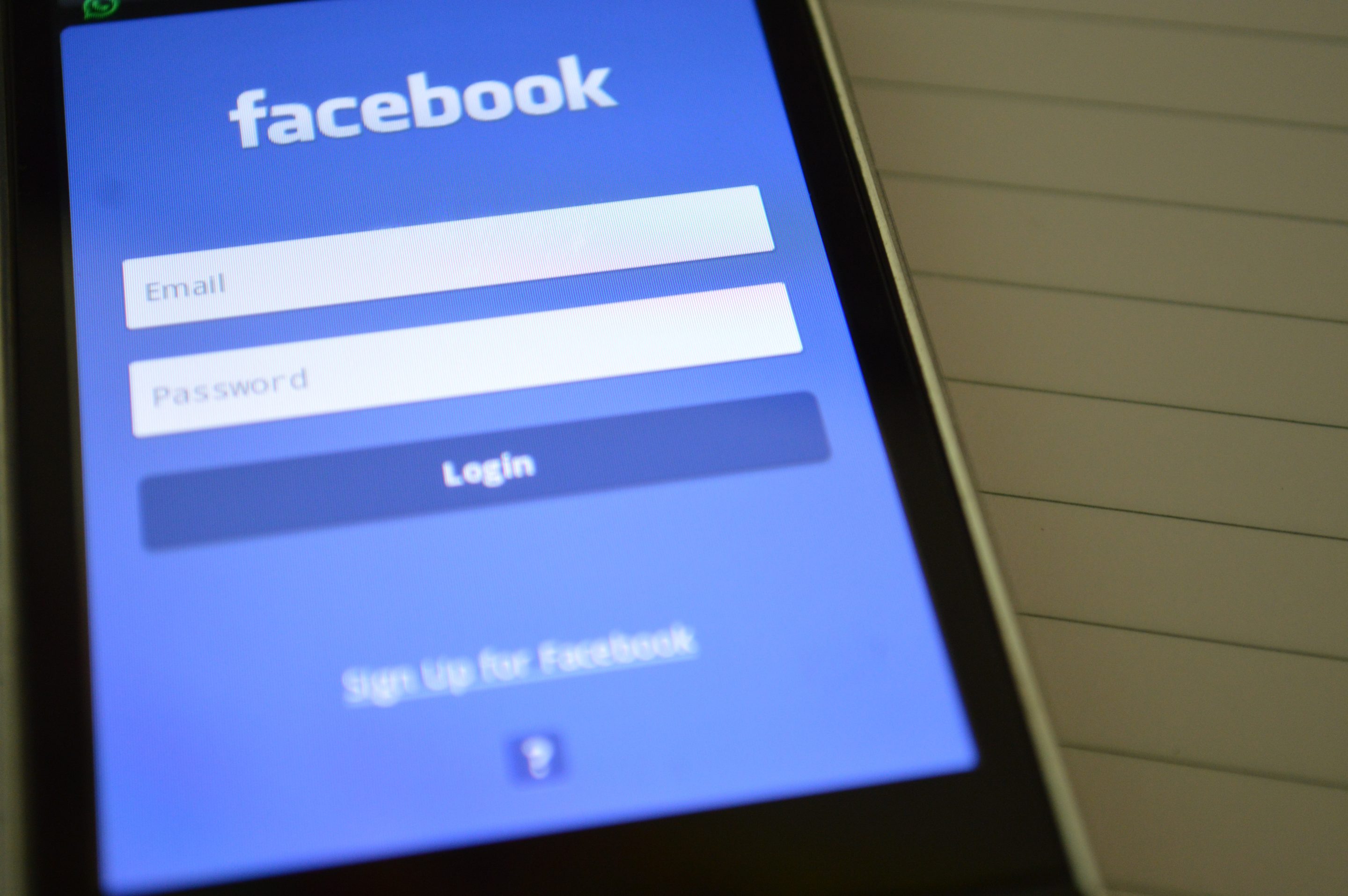 A cell phone is displaying a Facebook login screen, targeting the ideal audience for Facebook advertising.
