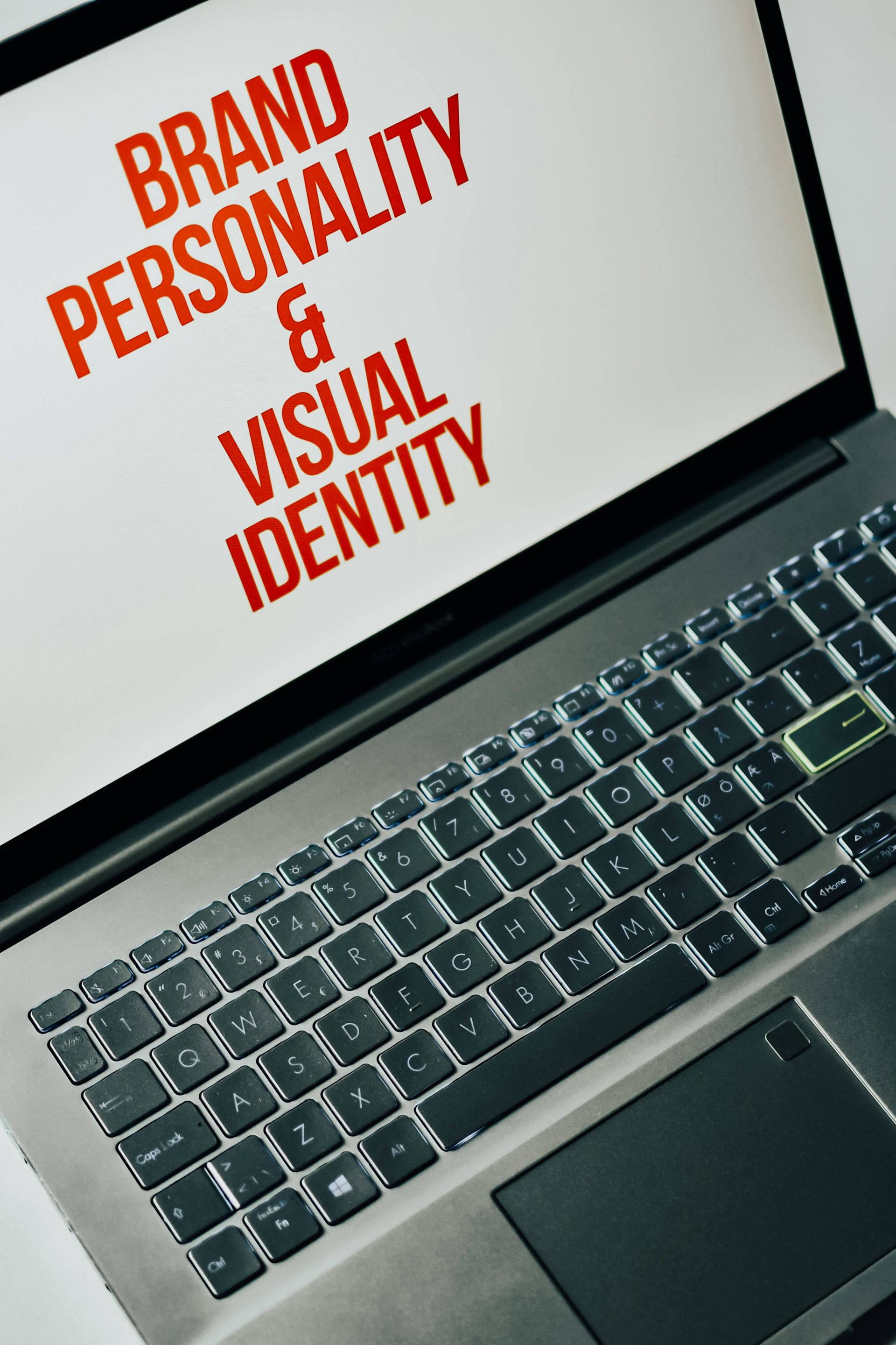 Laptop screen displaying the words "brand personality & visual identity" in red font, with a close-up of the keyboard visible.